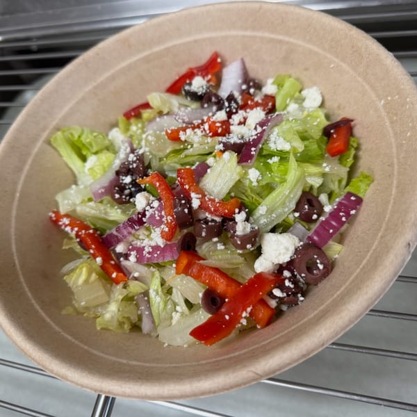 A fresh salad with lettuce, red peppers, red onions, black olives, and feta cheese in a bowl.