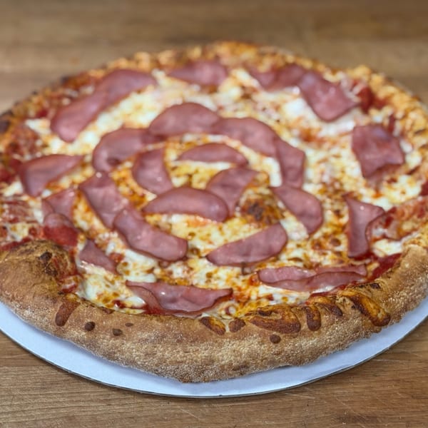A whole No Name Pizza with a golden crust, melted cheese, and sliced ham on a wooden table.