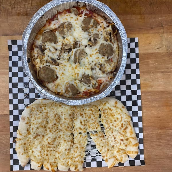 Baked spaghetti with meatballs and mushrooms in a foil pan, next to cheesy garlic bread.